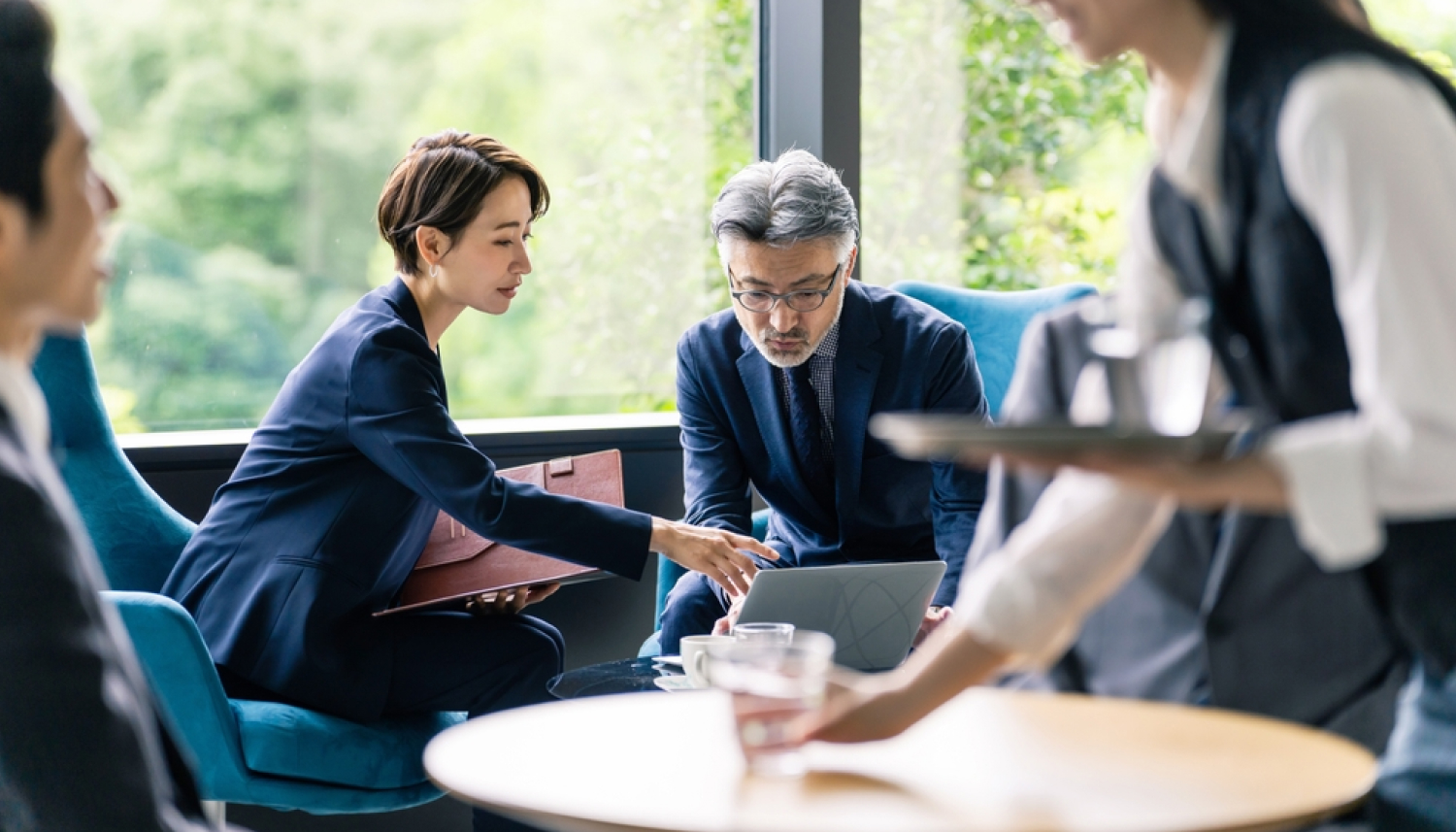 パソコンを見ながら打ち合わせするメガネをかけたスーツ姿の男性とショートヘアの女性