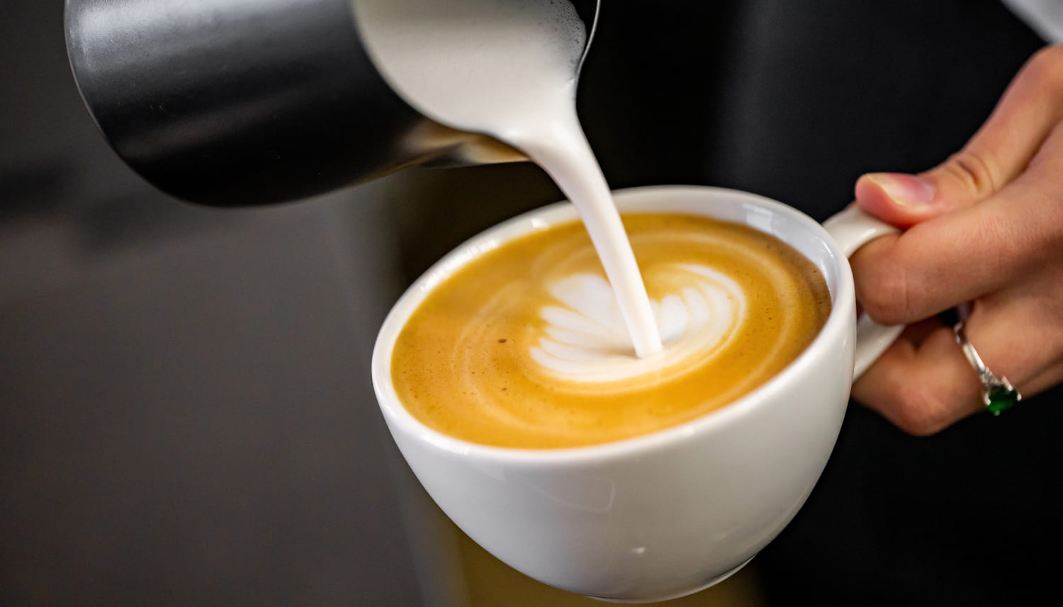 バリスタがコーヒーに蒸しミルクを注ぎ、美しいラテアートのデザインを作り出す様子