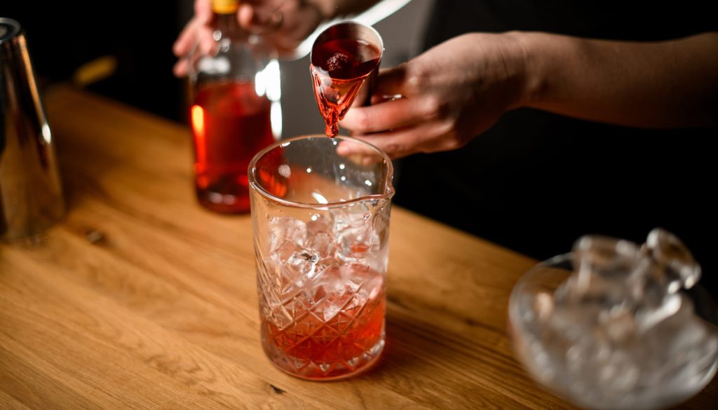 氷でカクテルガラスに茶色の液体のジガーを注ぐバーテンダーの女性の手
