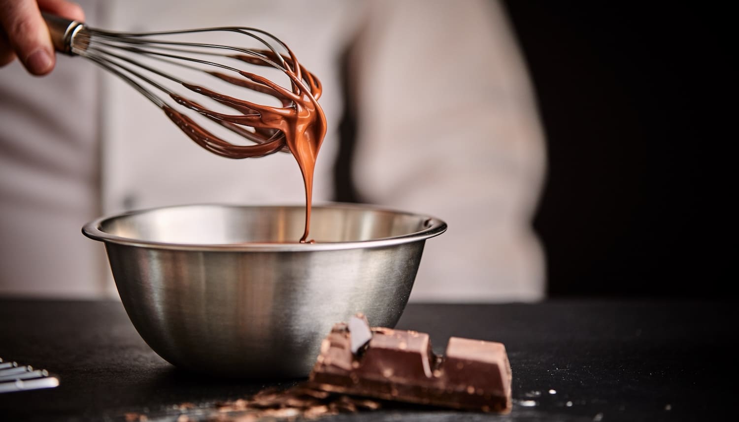 ボールに入ったチョコレートを泡立て器ですくってる写真