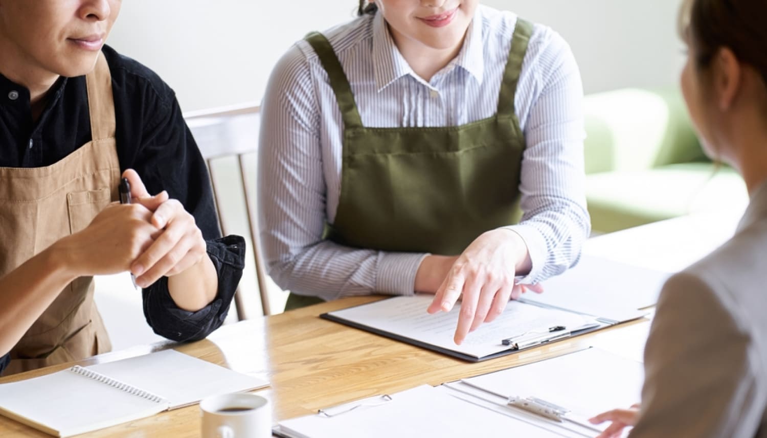 打ち合わせをするエプロン姿の男性と女性で手前側にスーツを着た女性
