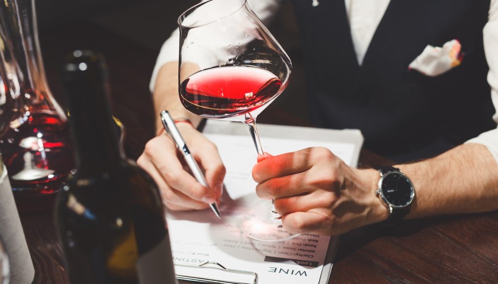 ワイングラスを持ちながら書類に記載しているソムリエの男性