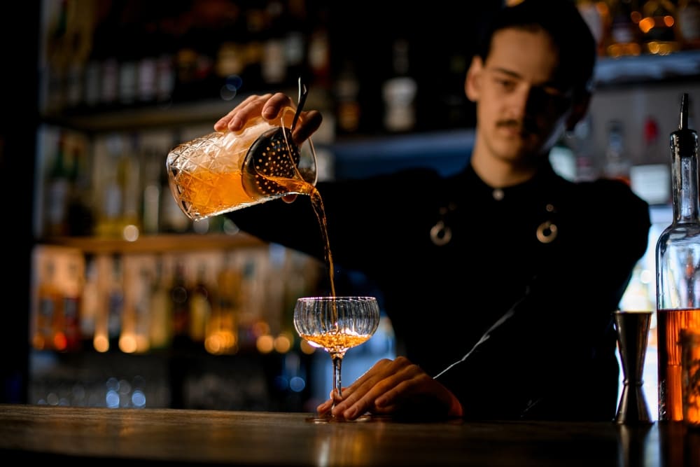 グラスにカクテルを注ぐイケメン男性バーテンダー