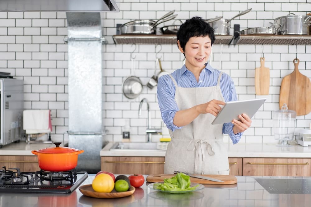 キッチンでタブレットを触るエプロンをかけた女性