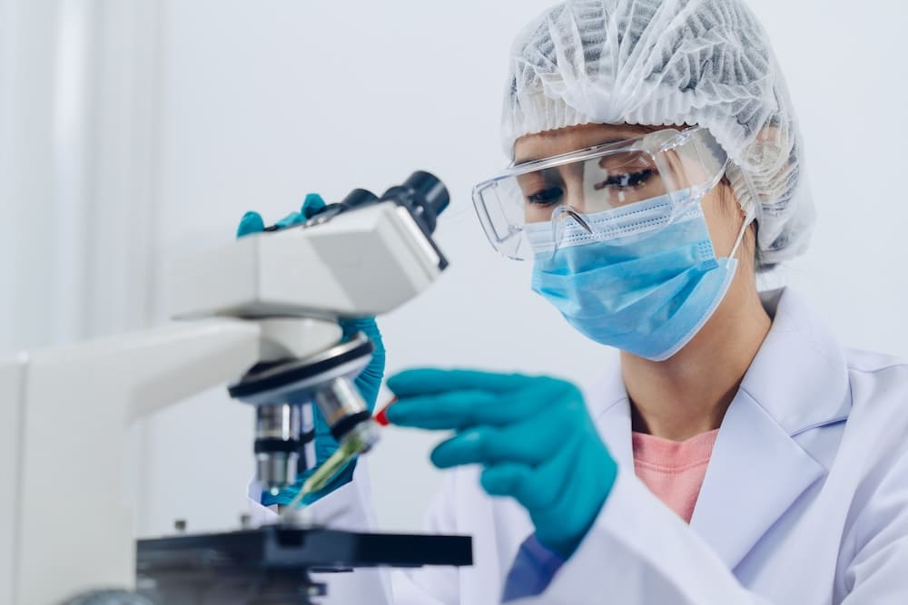 白衣とマスクをつけて顕微鏡で検査をする女性衛生士