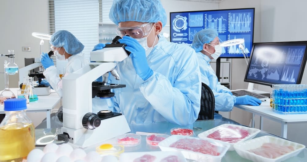 顕微鏡を覗く青いユニフォームを着た男性研究員