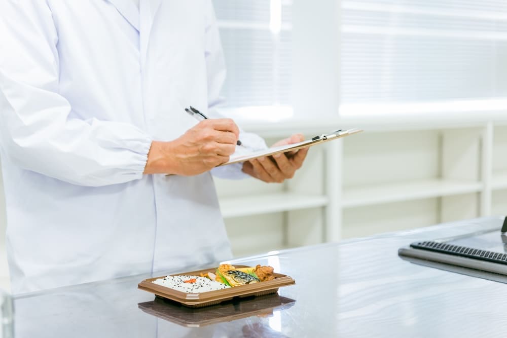 お弁当の食品を検査する白衣を着た男性