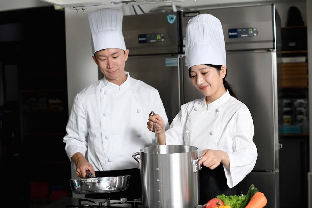 鍋で煮込む女性シェフと見守る男性シェフ