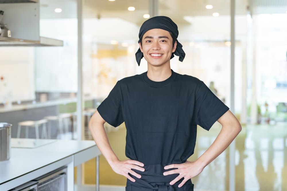 厨房で両手を腰に当てた頭にタオルを巻いた若い男性