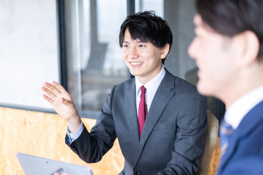 パソコンを見ながら話をするスーツを着た男性