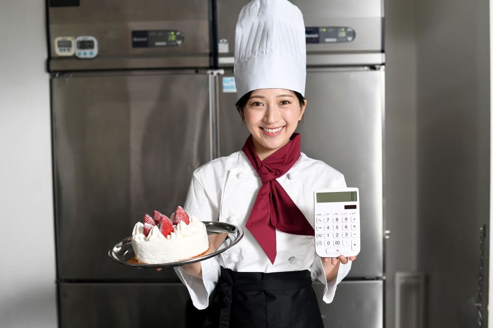 電卓とショートケーキを持った女性のパティシエ