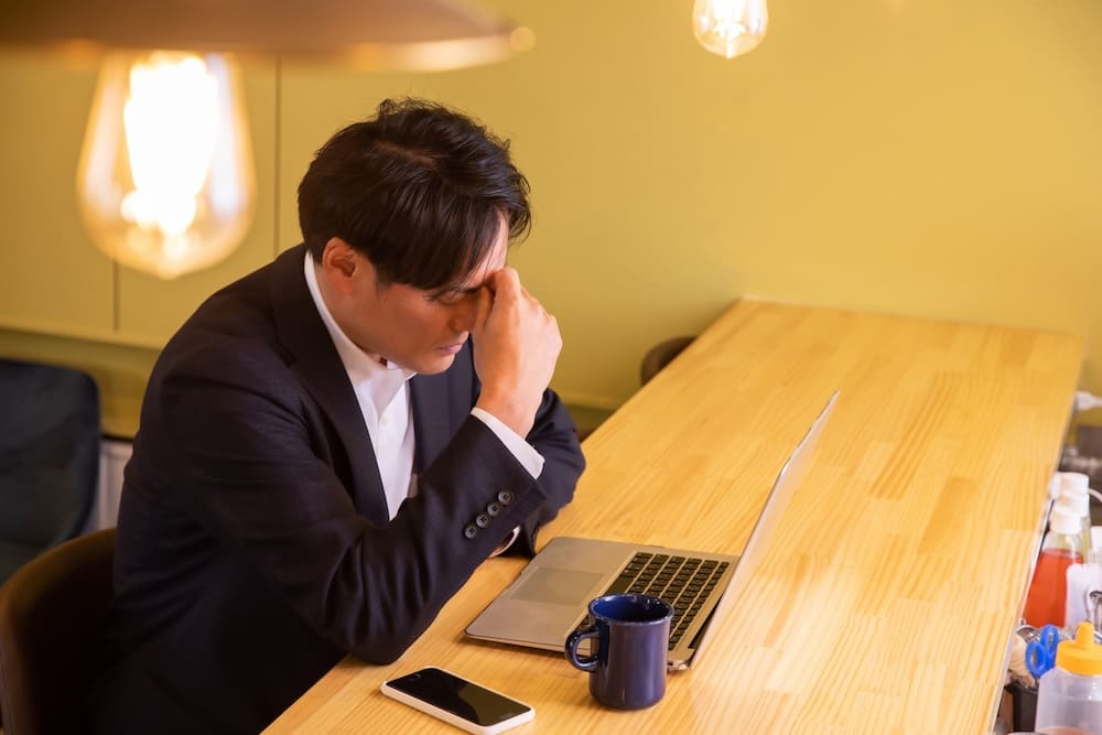 パソコンを見ながら眉間を摘む男性
