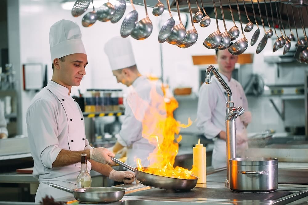 炎が上がるフライパンで調理する男性