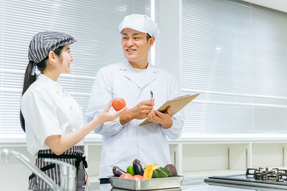 トマトを持つ女性店員と白衣を着た衛生士の男性