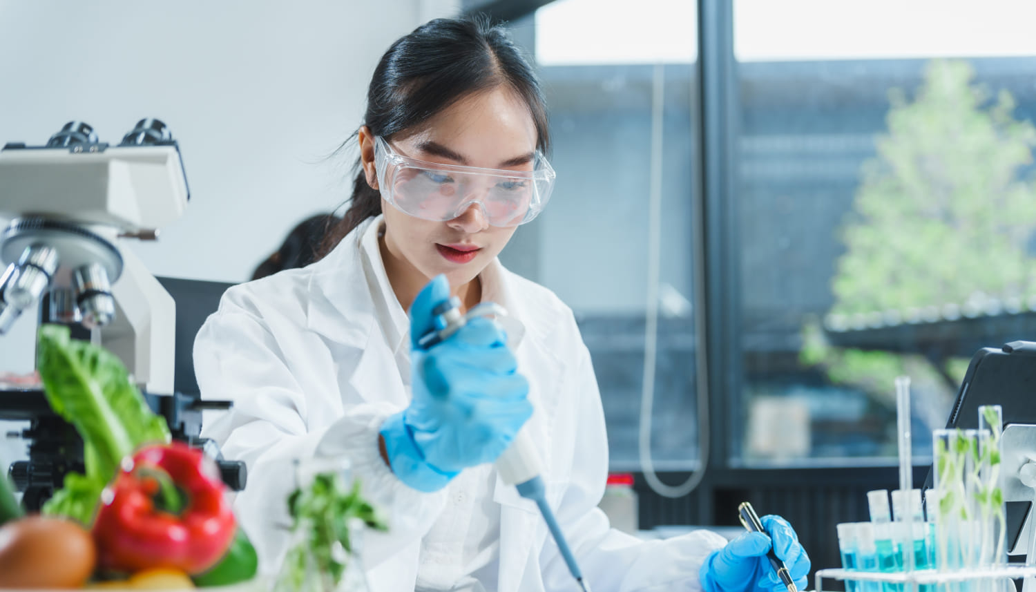 アジア人女性が、顕微鏡、シャーレ、試験管に化学溶液を充填して食品研究に取り組んでいる