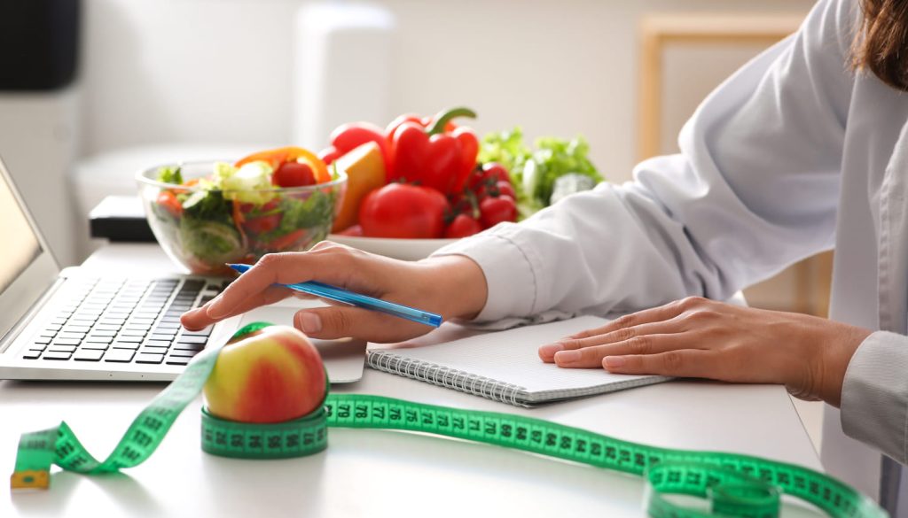 オフィスのテーブルでノートパソコンと食材を扱う若い女性