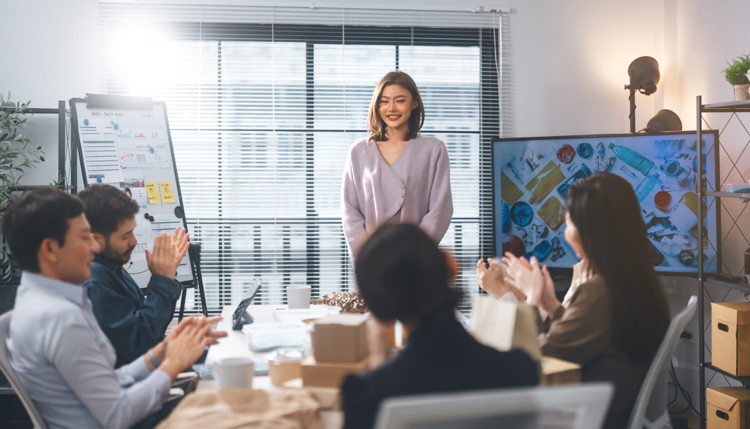 数人のテーブルに座った男女と彼らにモニターを使ってプレゼンする女性