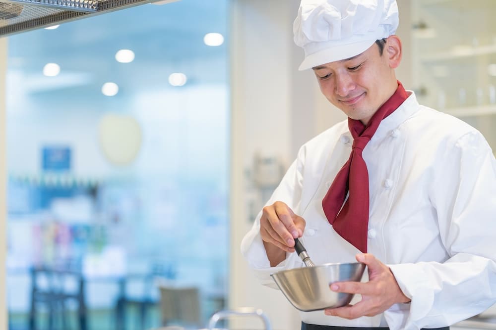 泡立て器でボールの中身を混ぜる男性シェフ