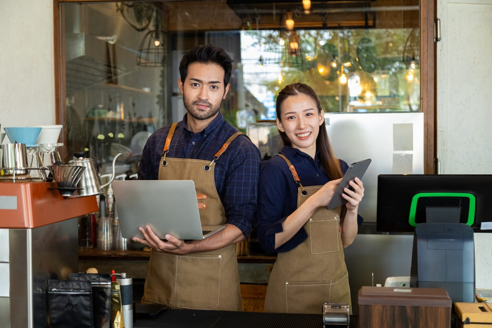 エプロンをかけたパソコン持つ男性と伝票を持つ女性