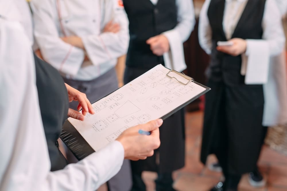 バインダーの書類を見ながら話をする人と周りで話を聞くウェイトレス