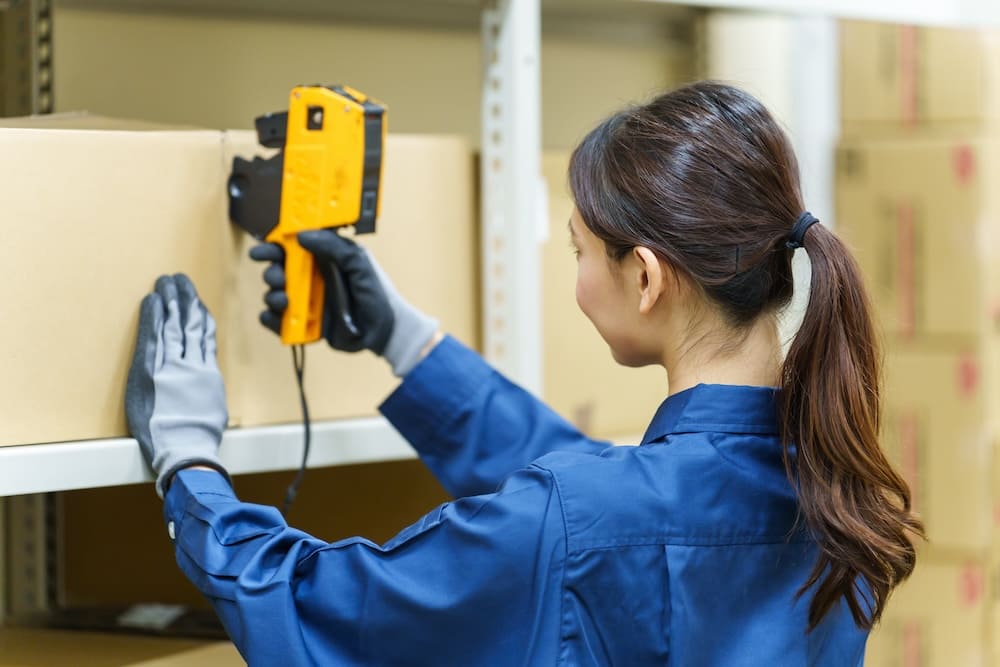 倉庫の段ボールを専用の機械で調べる女性作業員
