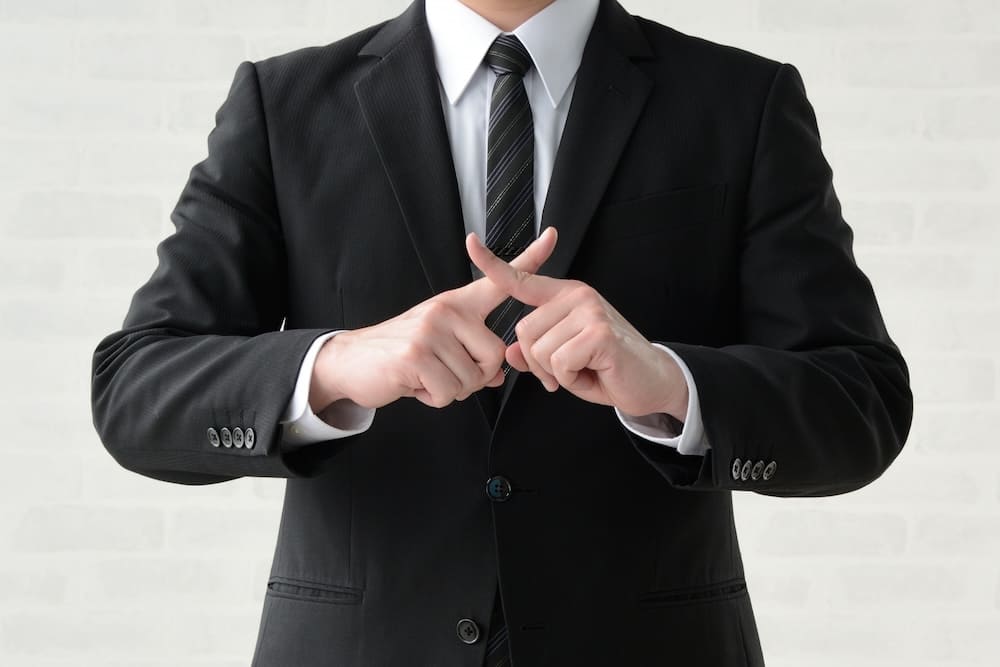 指で罰印を作っているスーツを着た男性の手元