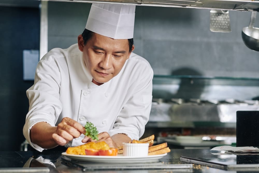 作った料理にパセリを盛り付けるアジア人のシェフ