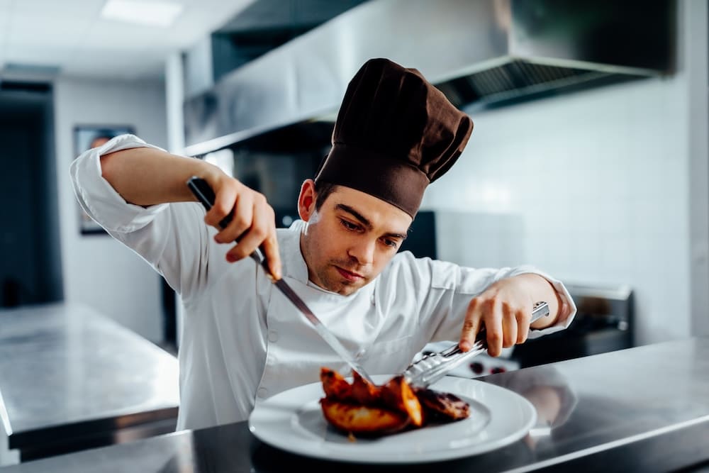お肉の料理をカットしている男性シェフ