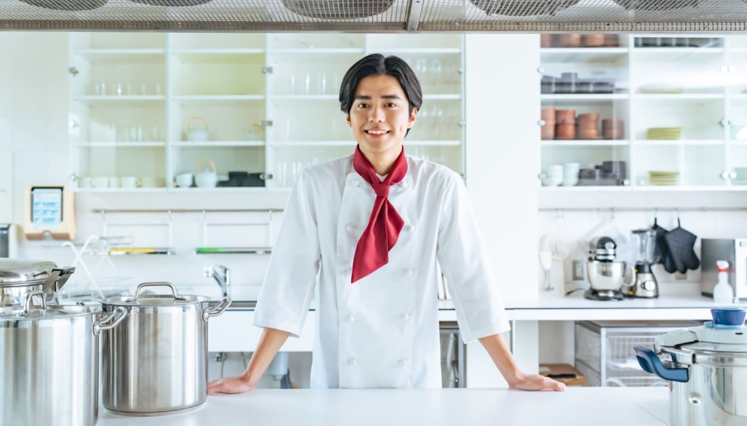 厨房のテーブルに両手をつく若い男性シェフ