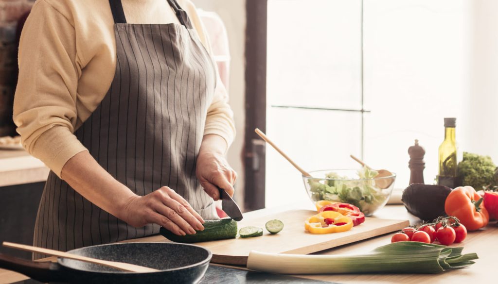 エプロンをかけてまな板で野菜を切る女性