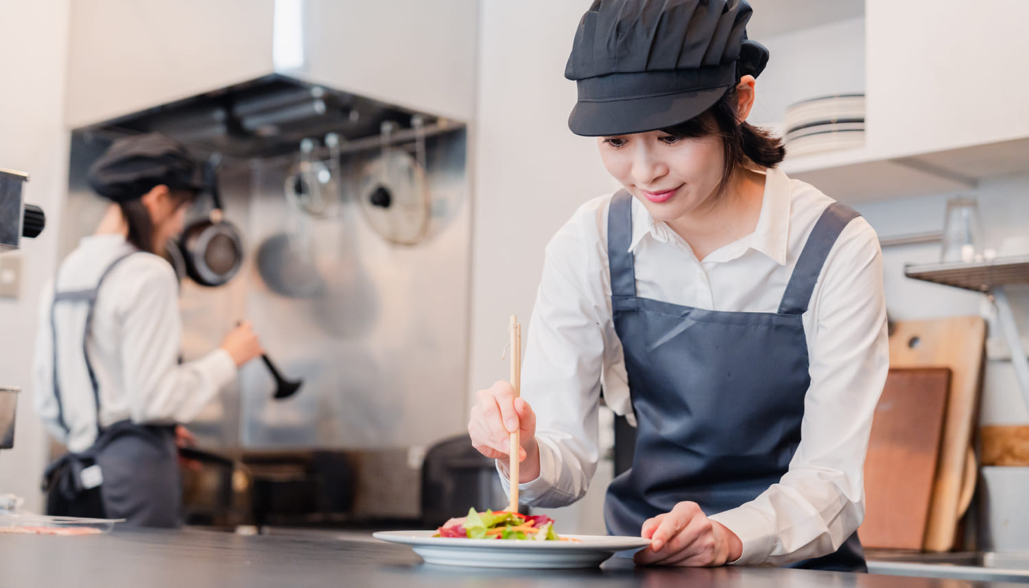 料理を盛り付けるキャップを被った女性店員