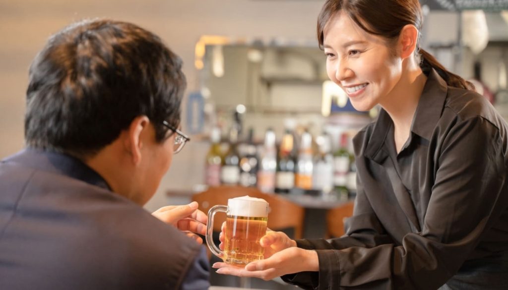 笑顔でサラリーマンの男性にビールを渡す女性店員