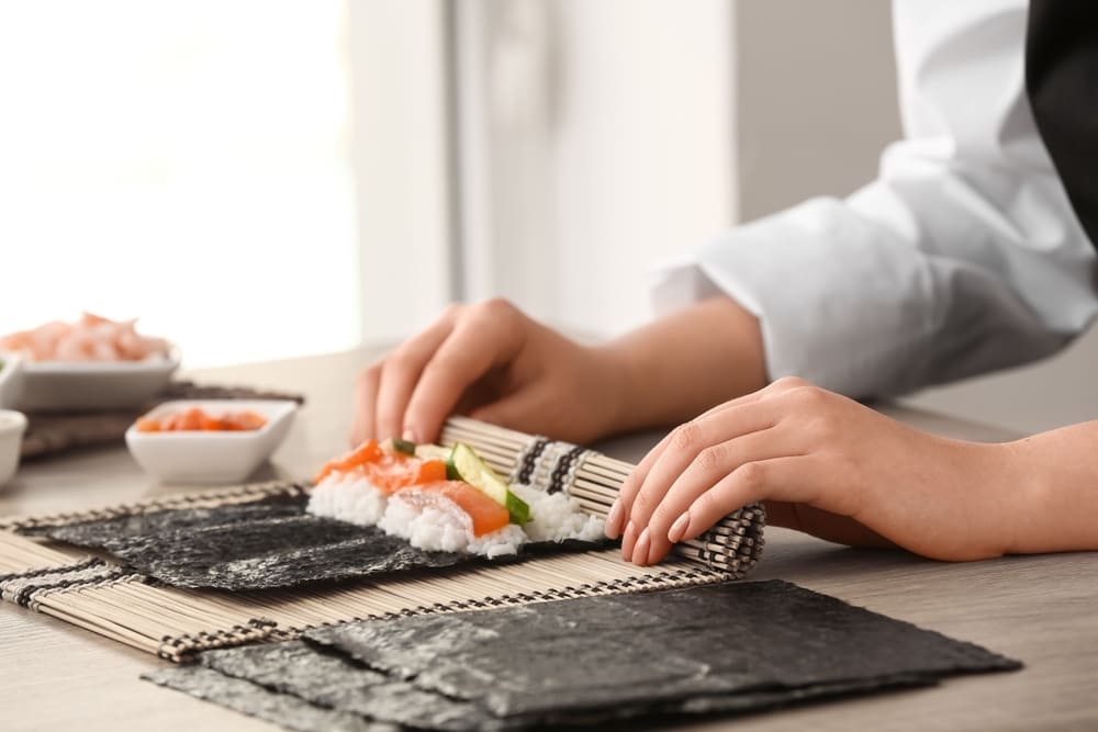 野菜とサーモンののった巻き寿司を作る女性