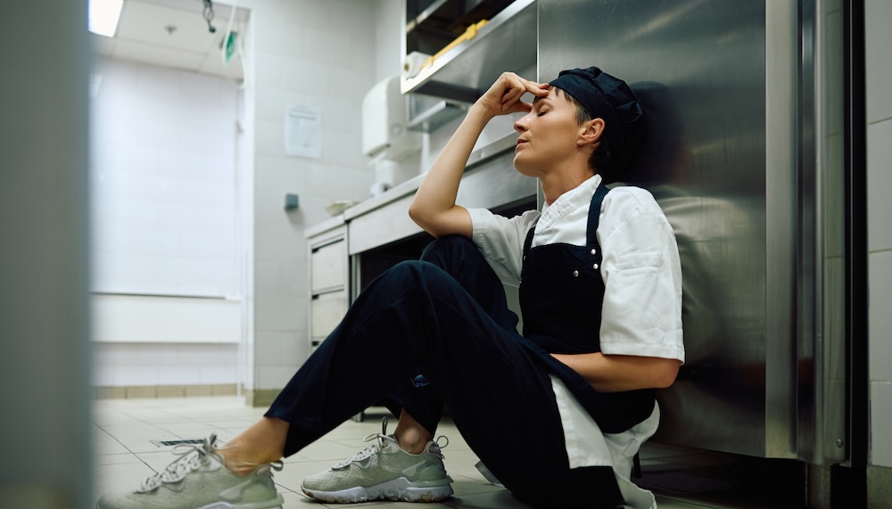 厨房にもたれかかって頭を抱える女性