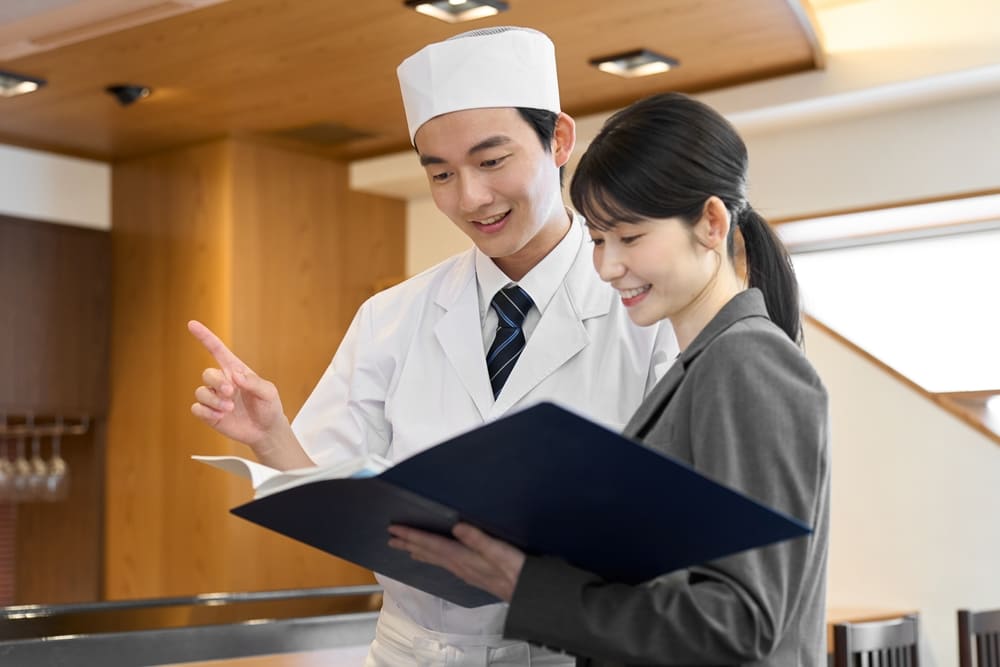 男性料理人と打ち合わせをするスーツを着た女性