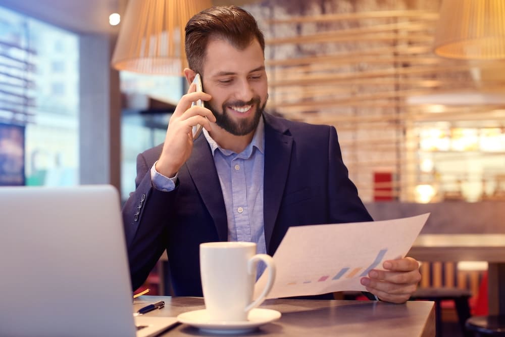 飲食店で電話をしながらデータを見るスーツを着た男性