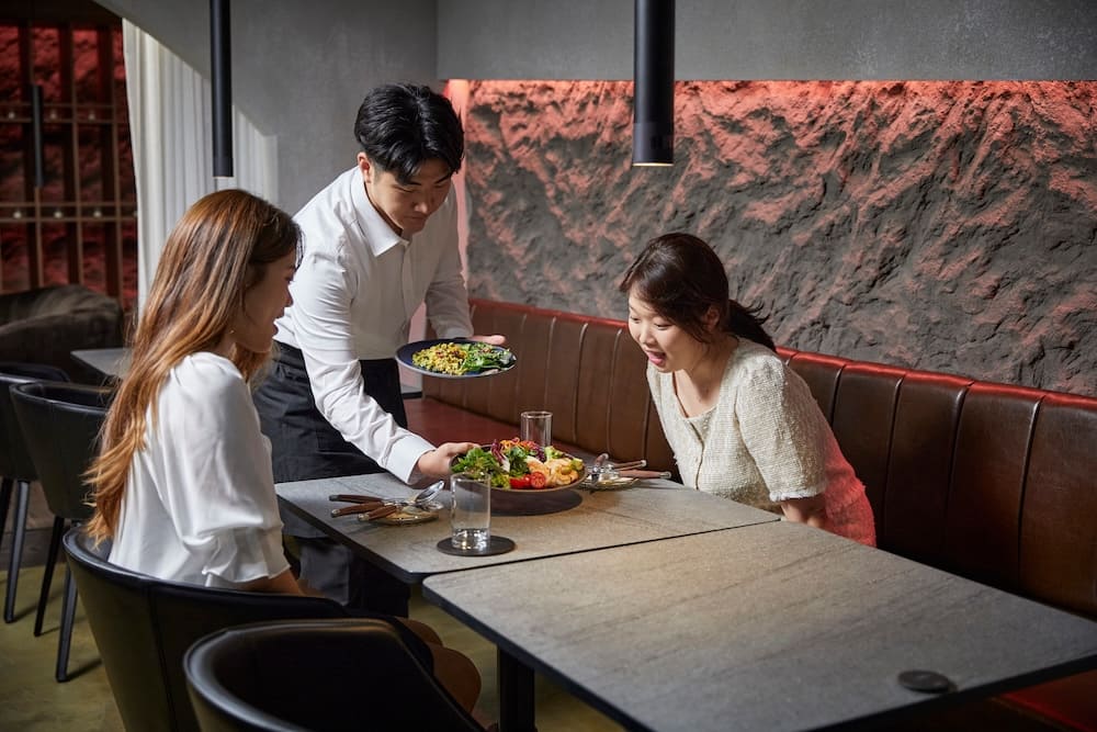 料理を配膳する男性とテーブルに座っている女性