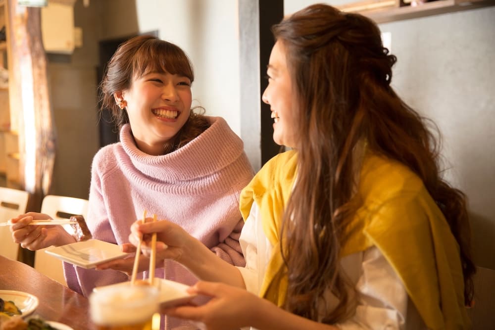 料理を食べながら笑顔で話す女性2人