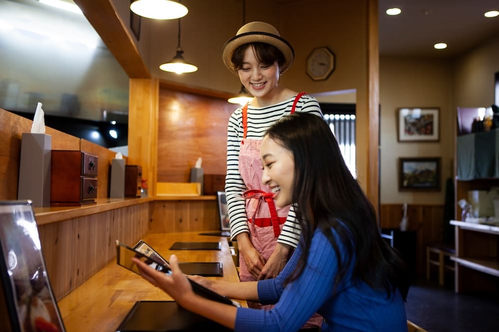 笑顔で接客する女性店員とメニューを見る女性のお客