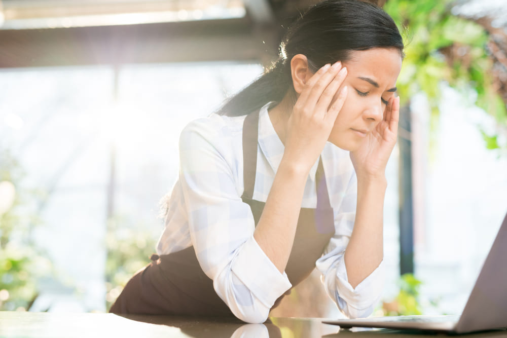 頭を抱えるエプロンをつけた女性店員