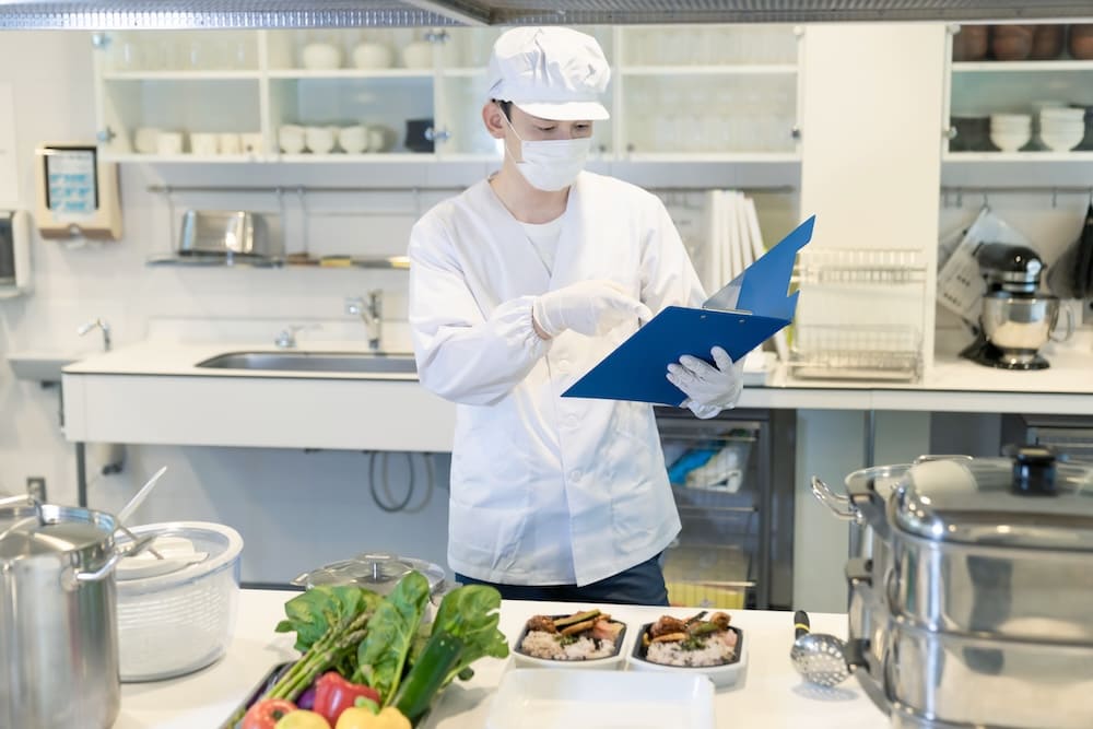 書類を見ながら食材を選ぶ白衣を着た衛生士