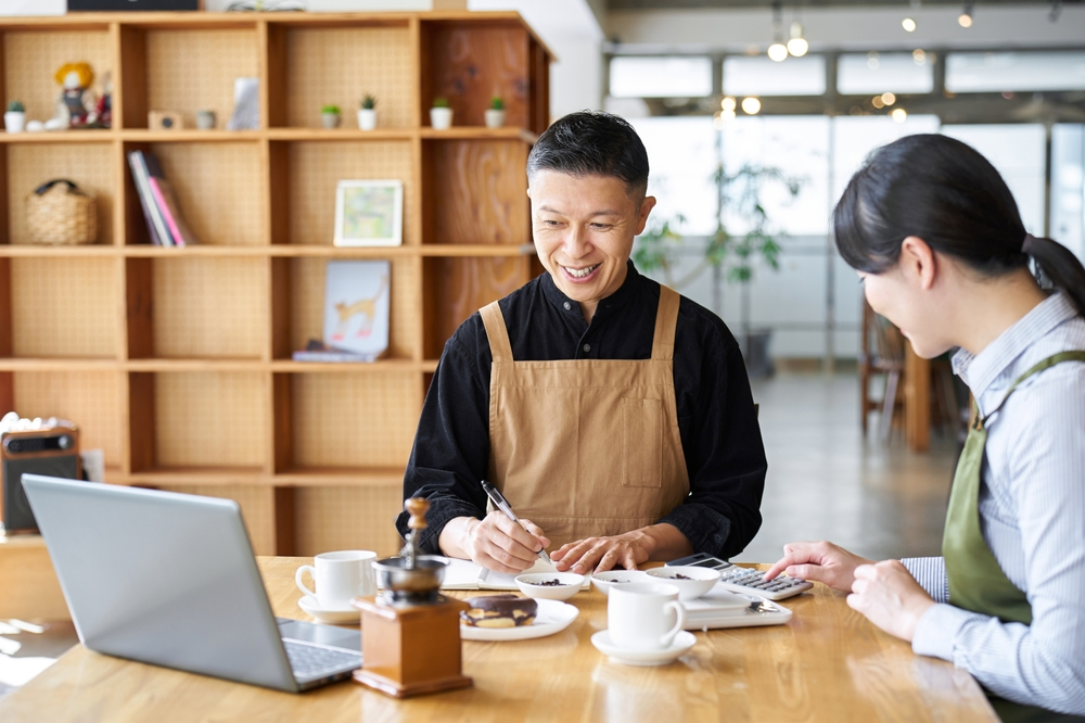 飲食店の男性スタッフと女性うスタッフが計算器を使ってミーティングしている様子
