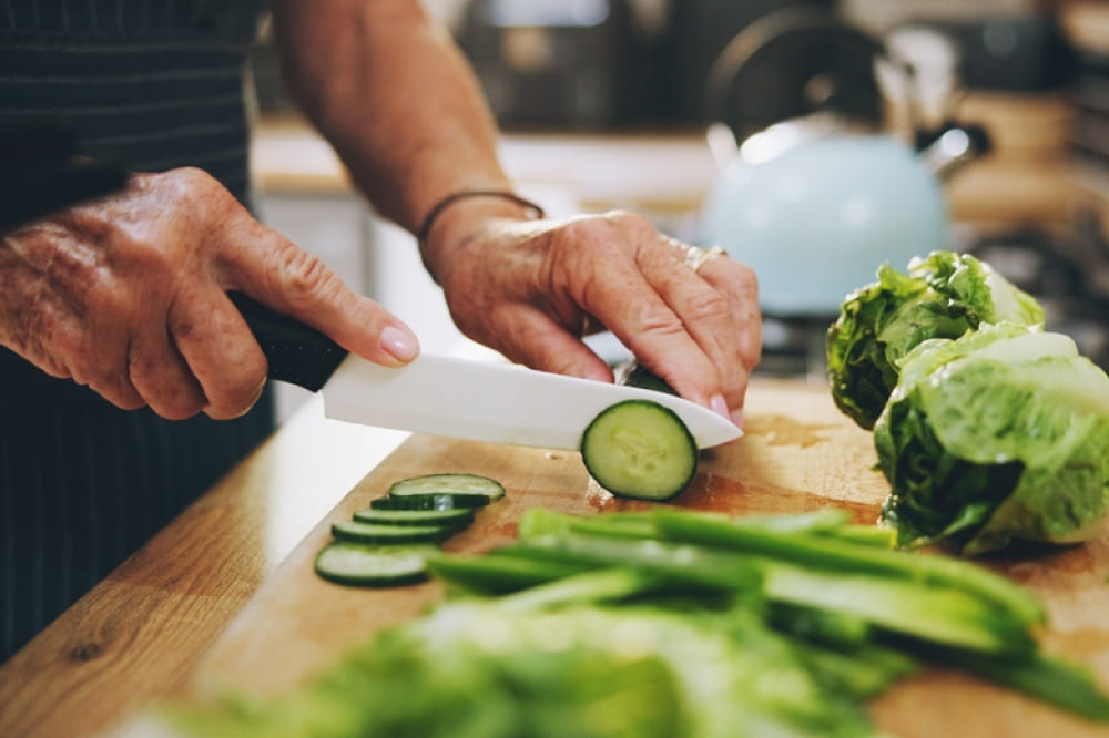 健康的な食べ物や栄養のための緑の野菜を持つキッチンの手、まな板、サラダ。