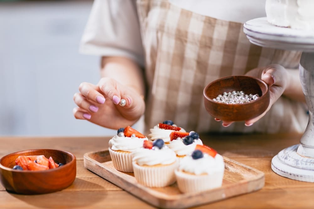 パティシエ菓子職人の若い女性が、キッチンテーブルの上に甘いボールキャンディケーキを飾る。