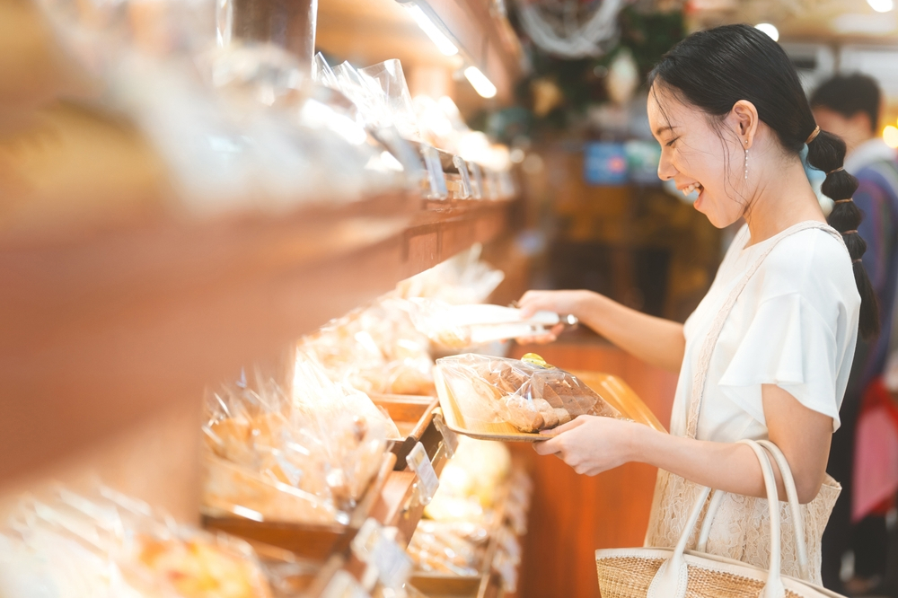 幸せな笑顔の顧客パン屋でパンを選ぶアジアの女性。全粒焼き日用品と人物のライフスタイル。